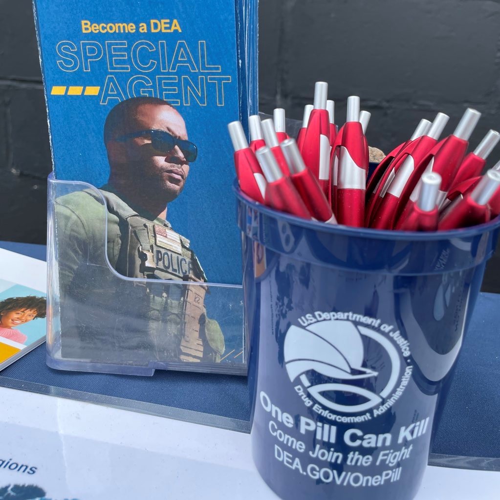 A blue DEA cup with red pens next to a recruiting brochure.