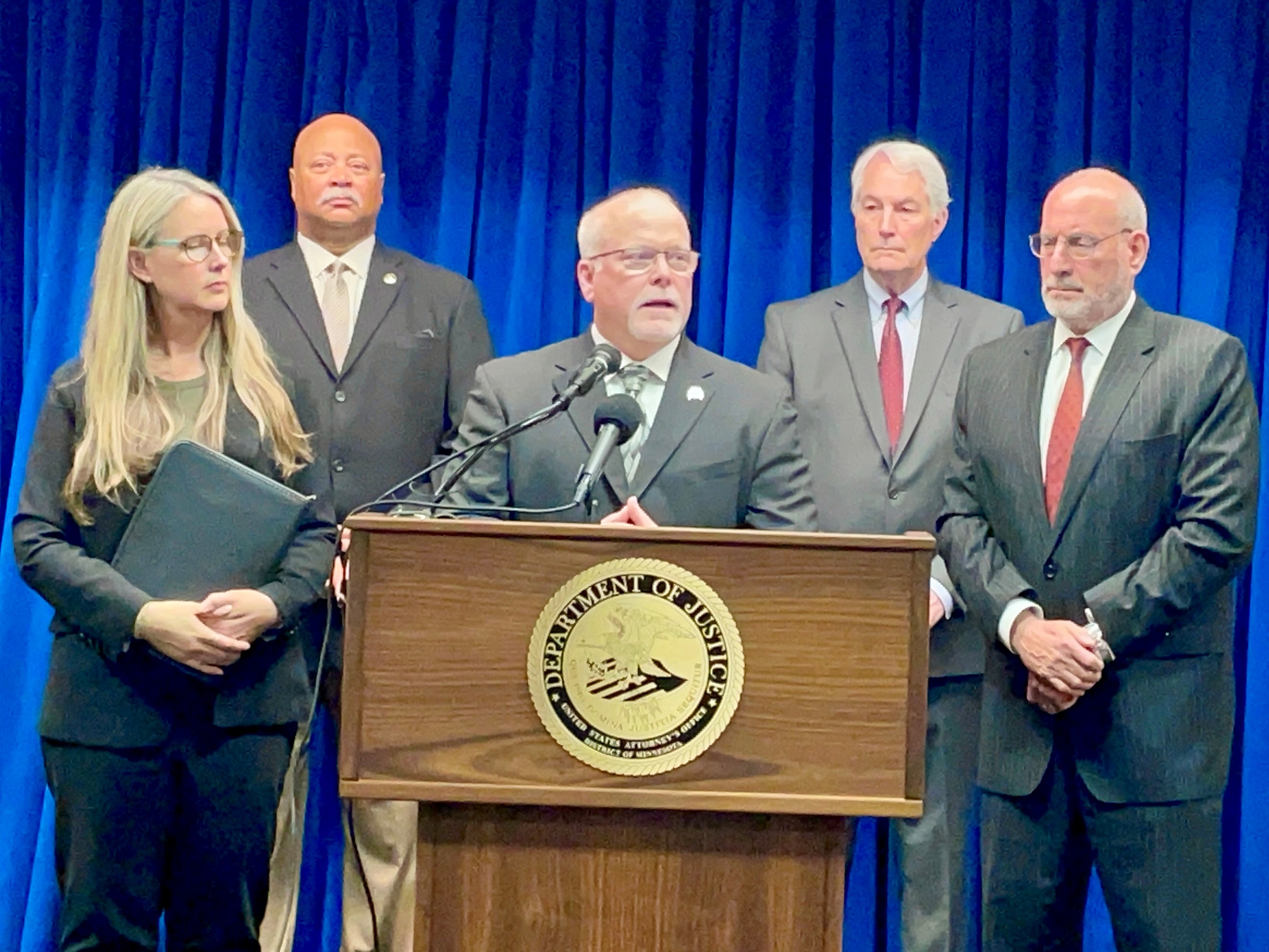 Members of the FBI, U.S. Marshals, DEA and U.S. Attorney's Office for the District of Minnesota address media behind a podium.