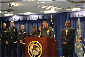 Associate SAC Briane Grey is speaking at the podium; ASAC Jon Goldberg is in the DEA jacket to his right, and US Attorney Andre Birotte is to his left at the press conference announcing the arrests.