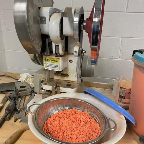 Pill press and bowl of orange pills 