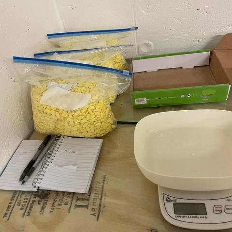 a scale, a notebook and pen, and 3 bags of yellow pills 