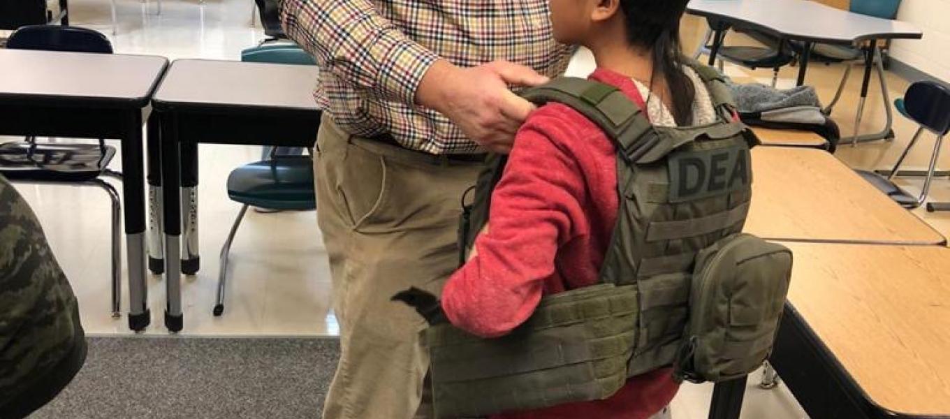 An agent with DEA helps a student try on a raid vest.