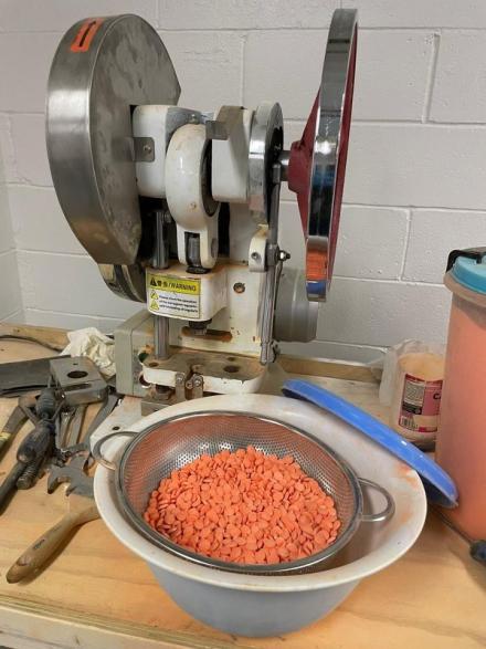 Pill press and bowl of orange pills