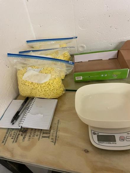 a scale, a notebook and pen, and 3 bags of yellow pills 